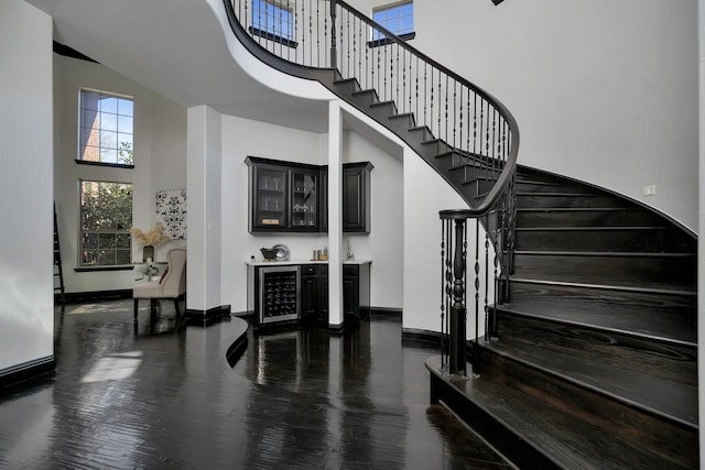 stairs with a dry bar, baseboards, a towering ceiling, wine cooler, and wood finished floors