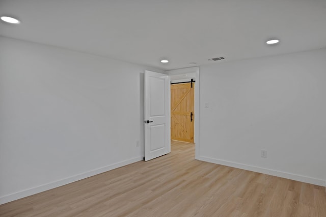 empty room featuring light wood-type flooring, visible vents, baseboards, and a barn door