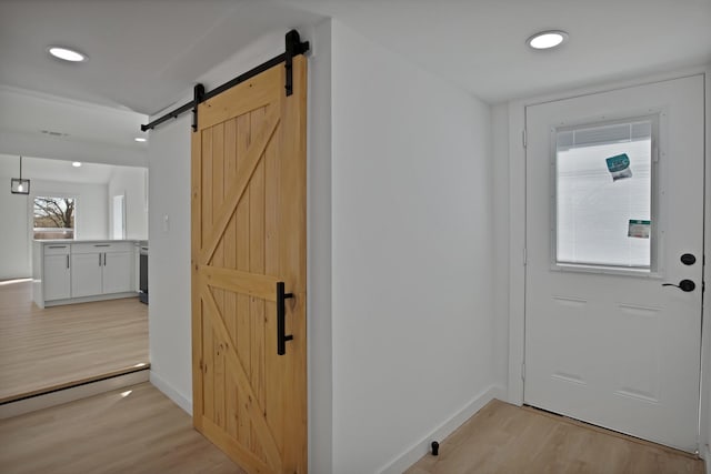 entryway with light wood finished floors, a barn door, baseboards, and recessed lighting