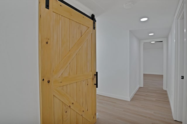 corridor with light wood-style floors, a barn door, baseboards, and recessed lighting