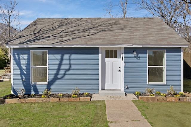 view of front of house with a shingled roof, a front yard, and an outbuilding