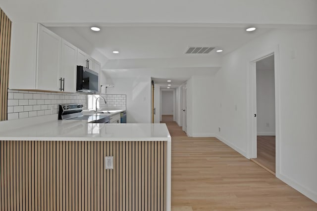 kitchen featuring electric range, decorative backsplash, light countertops, light wood-type flooring, and white cabinetry