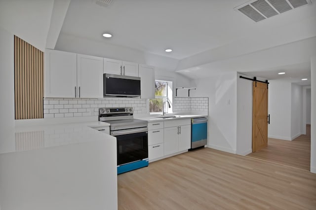 kitchen featuring a barn door, visible vents, stainless steel electric stove, light wood-style floors, and a sink