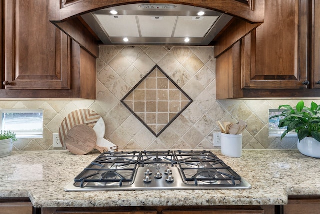 kitchen with stainless steel gas cooktop, tasteful backsplash, arched walkways, and custom exhaust hood