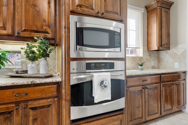 kitchen with brown cabinets, appliances with stainless steel finishes, light stone counters, and backsplash