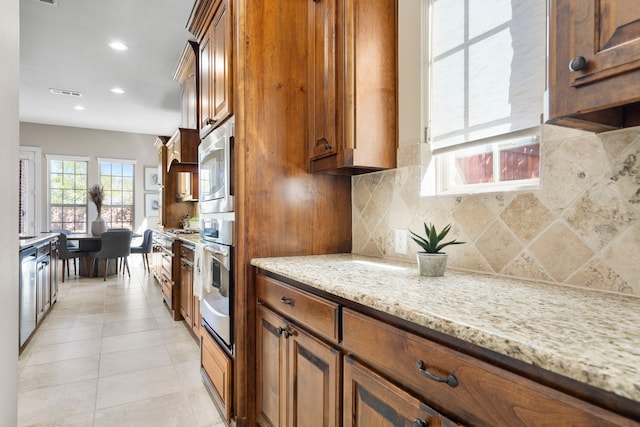 kitchen featuring light tile patterned floors, visible vents, decorative backsplash, light stone countertops, and brown cabinetry