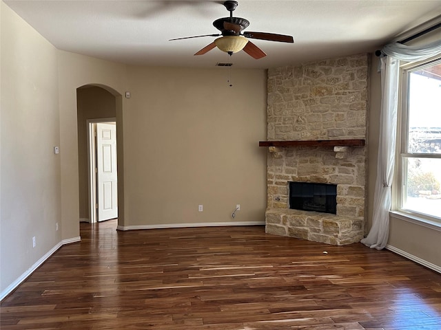 unfurnished living room featuring visible vents, arched walkways, a stone fireplace, and wood finished floors