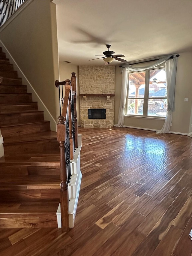 unfurnished living room with baseboards, ceiling fan, dark wood finished floors, stairs, and a fireplace