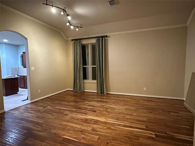 empty room with baseboards, wood finished floors, arched walkways, and ornamental molding