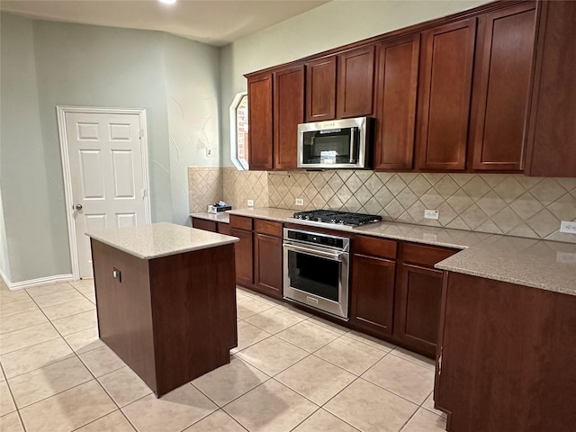 kitchen with light tile patterned floors, light stone counters, a kitchen island, decorative backsplash, and appliances with stainless steel finishes