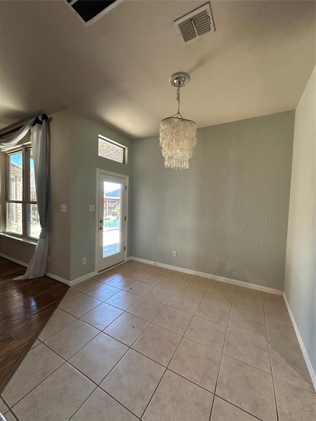 unfurnished dining area with light tile patterned floors, baseboards, visible vents, and a chandelier