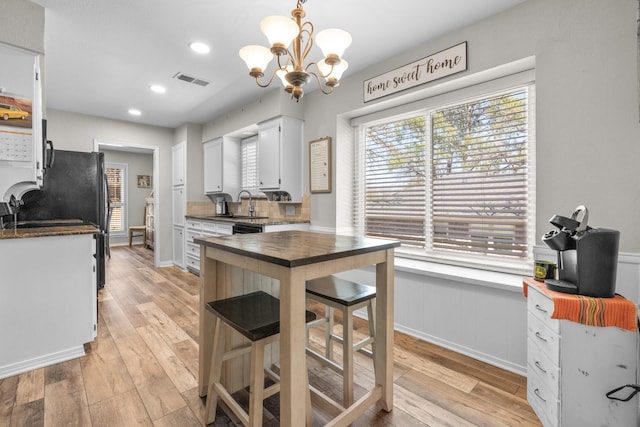 kitchen featuring light wood finished floors, white cabinetry, visible vents, and a wainscoted wall