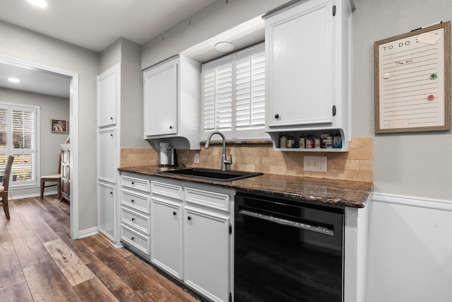 kitchen featuring black dishwasher, tasteful backsplash, white cabinets, dark wood-type flooring, and a sink