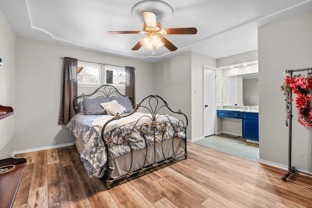 bedroom with light wood-style floors, ensuite bath, baseboards, and ceiling fan