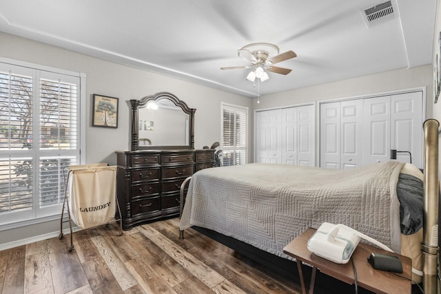 bedroom featuring two closets, visible vents, a ceiling fan, wood finished floors, and baseboards