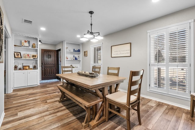 dining space with baseboards, light wood-style flooring, visible vents, and a notable chandelier