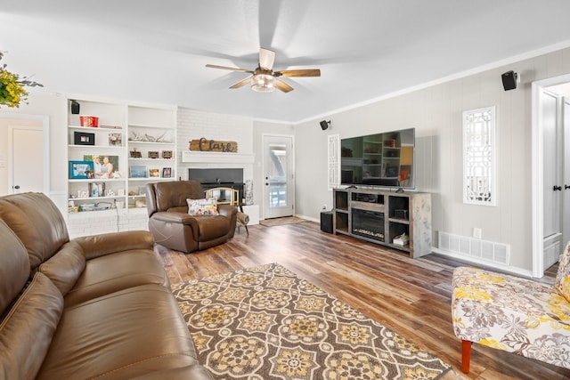 living area with a brick fireplace, wood finished floors, visible vents, and crown molding