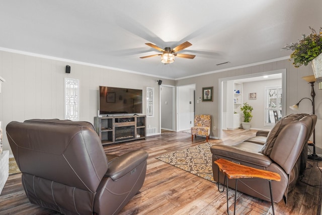 living room featuring ceiling fan, wood finished floors, visible vents, baseboards, and crown molding