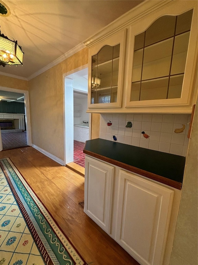 interior space featuring wood finished floors, backsplash, dark countertops, glass insert cabinets, and crown molding