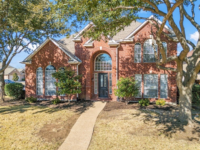 traditional home featuring a shingled roof, a front lawn, and brick siding