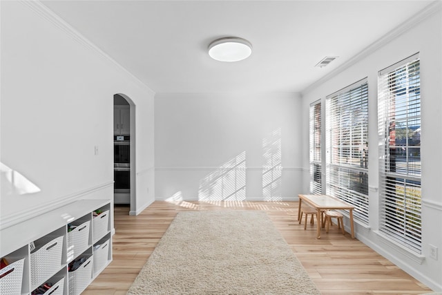 empty room featuring ornamental molding, arched walkways, light wood-style floors, and baseboards