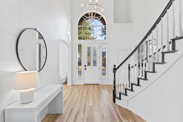 entrance foyer with light wood-style flooring, a notable chandelier, a towering ceiling, baseboards, and stairs