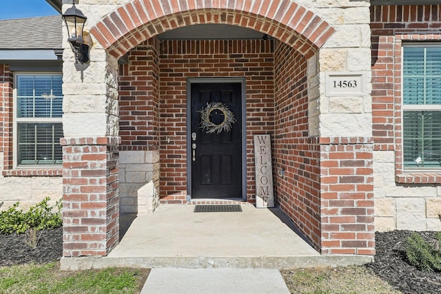 view of exterior entry featuring roof with shingles and brick siding