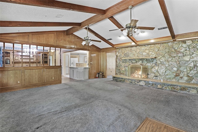 unfurnished living room featuring carpet, vaulted ceiling with beams, a fireplace, wooden walls, and a textured ceiling