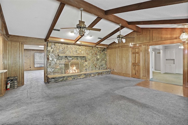 unfurnished living room with wooden walls, carpet, a stone fireplace, and lofted ceiling with beams