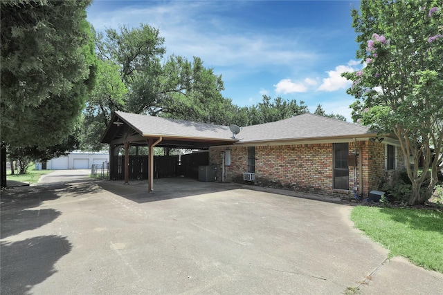 single story home featuring an outbuilding, brick siding, central air condition unit, a shingled roof, and a carport