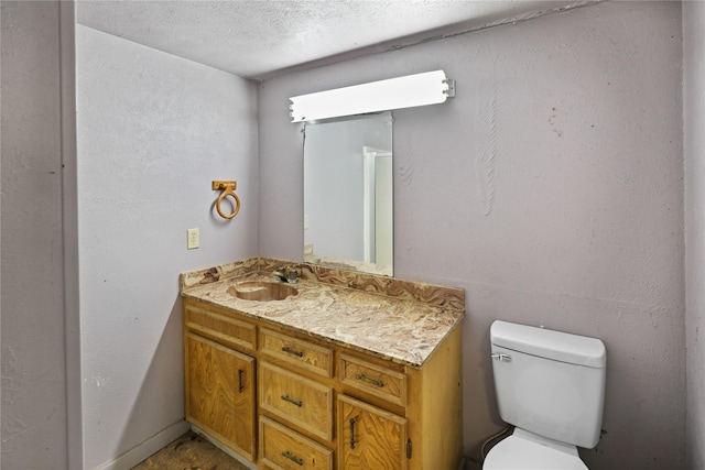 half bath with a textured ceiling, a textured wall, vanity, and toilet