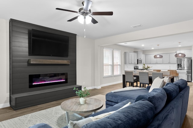 living area with a large fireplace, visible vents, light wood-style flooring, and baseboards