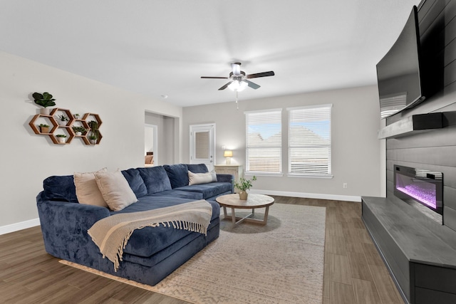 living room with ceiling fan, baseboards, wood finished floors, and a glass covered fireplace