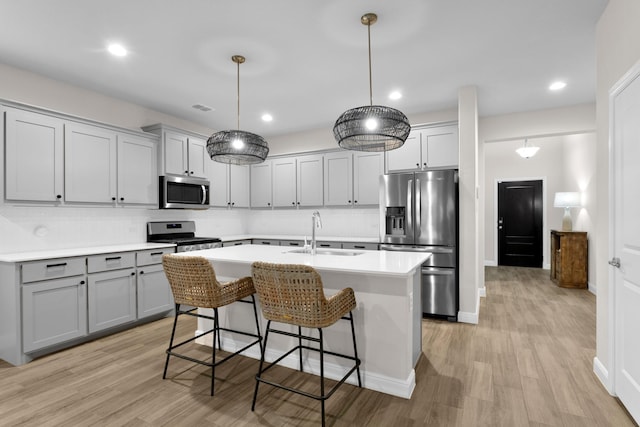 kitchen featuring a center island with sink, stainless steel appliances, light countertops, gray cabinetry, and a sink