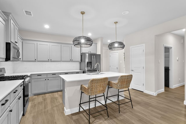 kitchen featuring a center island with sink, light wood-style flooring, gray cabinets, stainless steel appliances, and light countertops