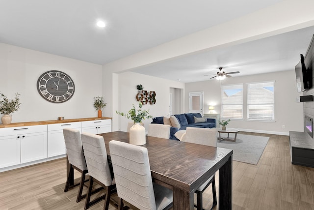 dining room featuring light wood-type flooring, baseboards, a ceiling fan, and a glass covered fireplace