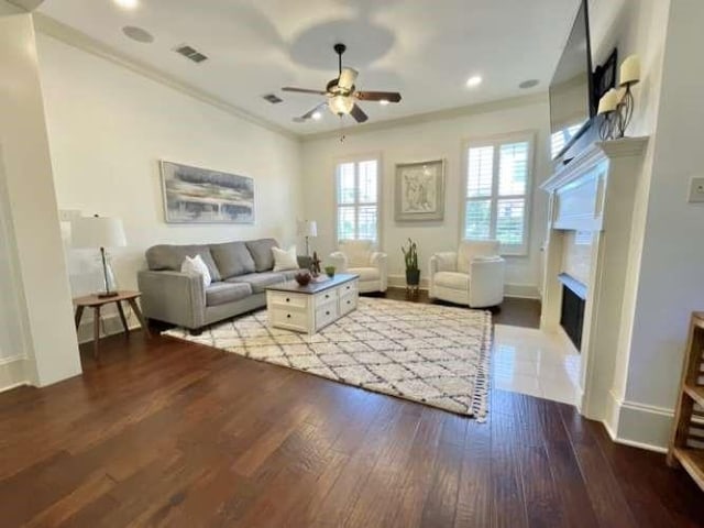 living area featuring a fireplace, visible vents, a ceiling fan, ornamental molding, and hardwood / wood-style floors