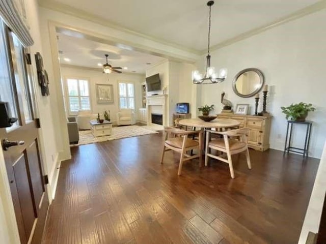 dining space with ceiling fan with notable chandelier, ornamental molding, a fireplace, and dark wood finished floors