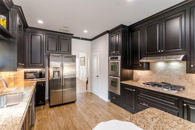 kitchen featuring stainless steel appliances, decorative backsplash, ornamental molding, a sink, and under cabinet range hood