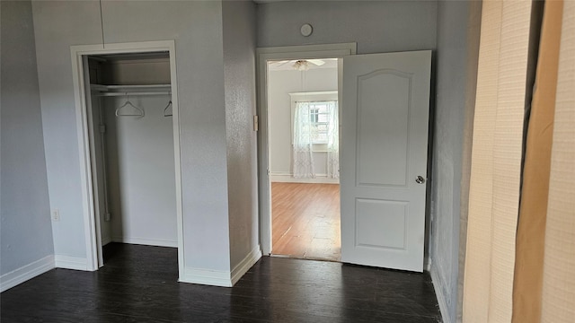 unfurnished bedroom featuring dark wood-style floors, baseboards, and a closet