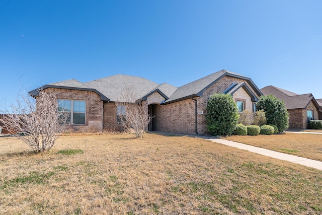 view of front of property with brick siding, roof with shingles, and a front yard