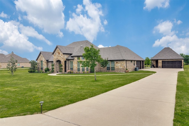 french country home with a garage, a shingled roof, an outdoor structure, stone siding, and a front yard