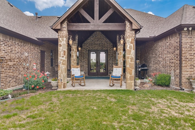 entrance to property with french doors, brick siding, a yard, and roof with shingles