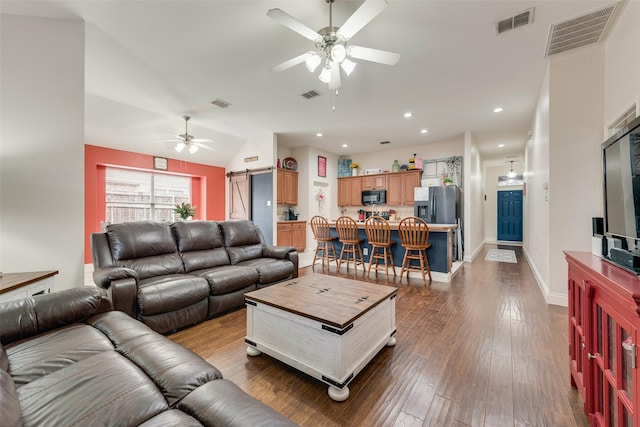 living room featuring a barn door, dark wood-style flooring, and visible vents