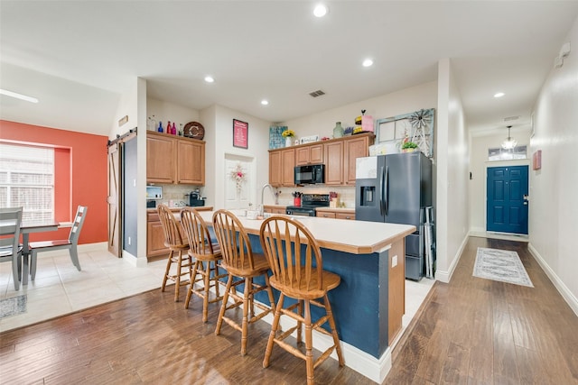 kitchen featuring a barn door, light wood-style flooring, light countertops, black appliances, and an island with sink