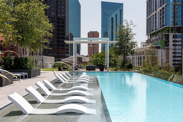 community pool with a patio area, fence, and a city view