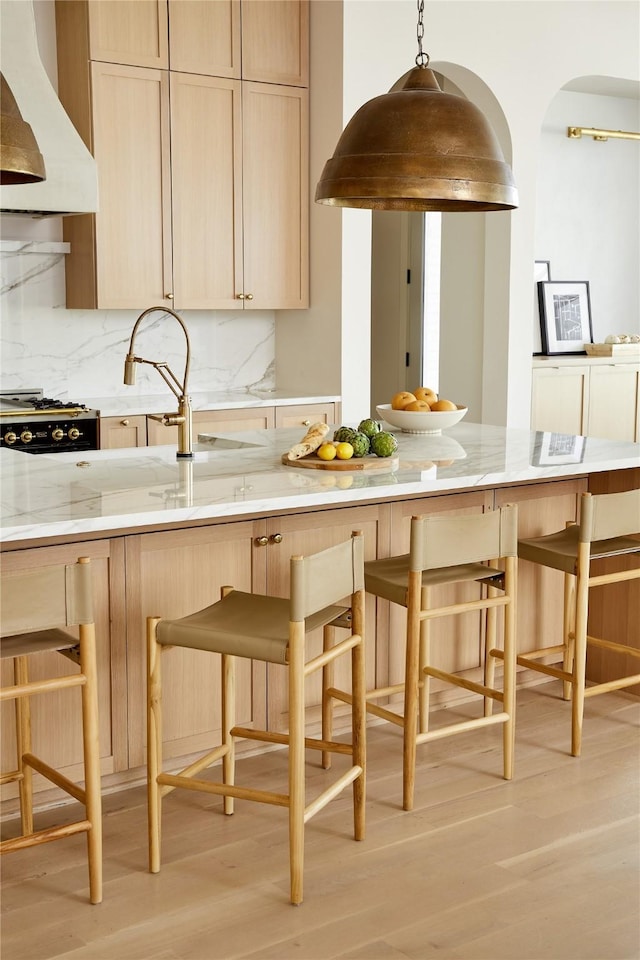 kitchen featuring tasteful backsplash, light brown cabinets, light wood finished floors, and custom exhaust hood