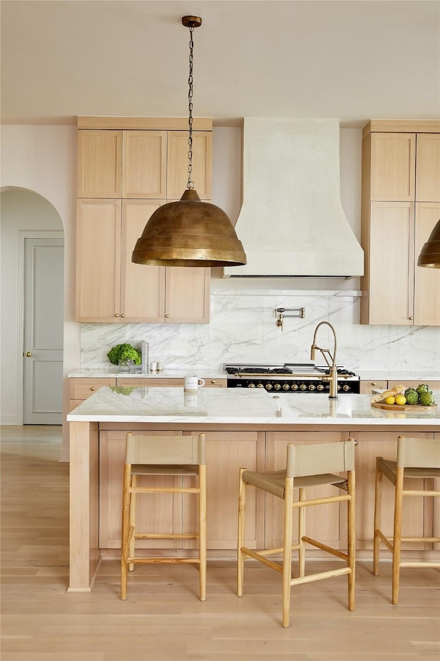 kitchen featuring tasteful backsplash, custom range hood, a kitchen breakfast bar, and light brown cabinetry