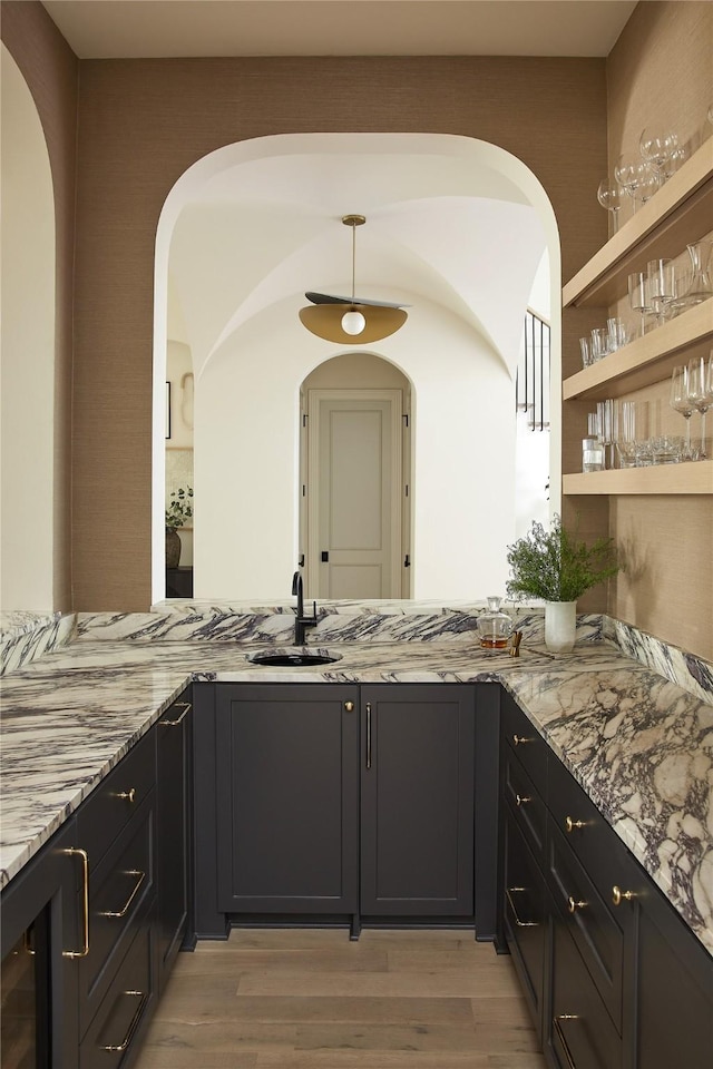 bar featuring hanging light fixtures, a sink, and light wood-style floors