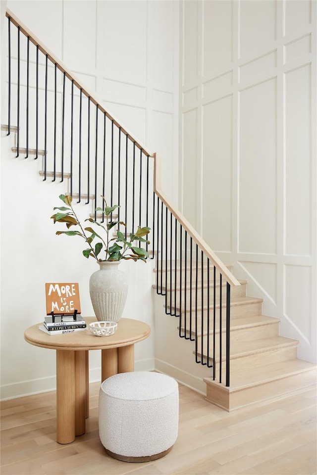 staircase featuring baseboards, a decorative wall, and wood finished floors